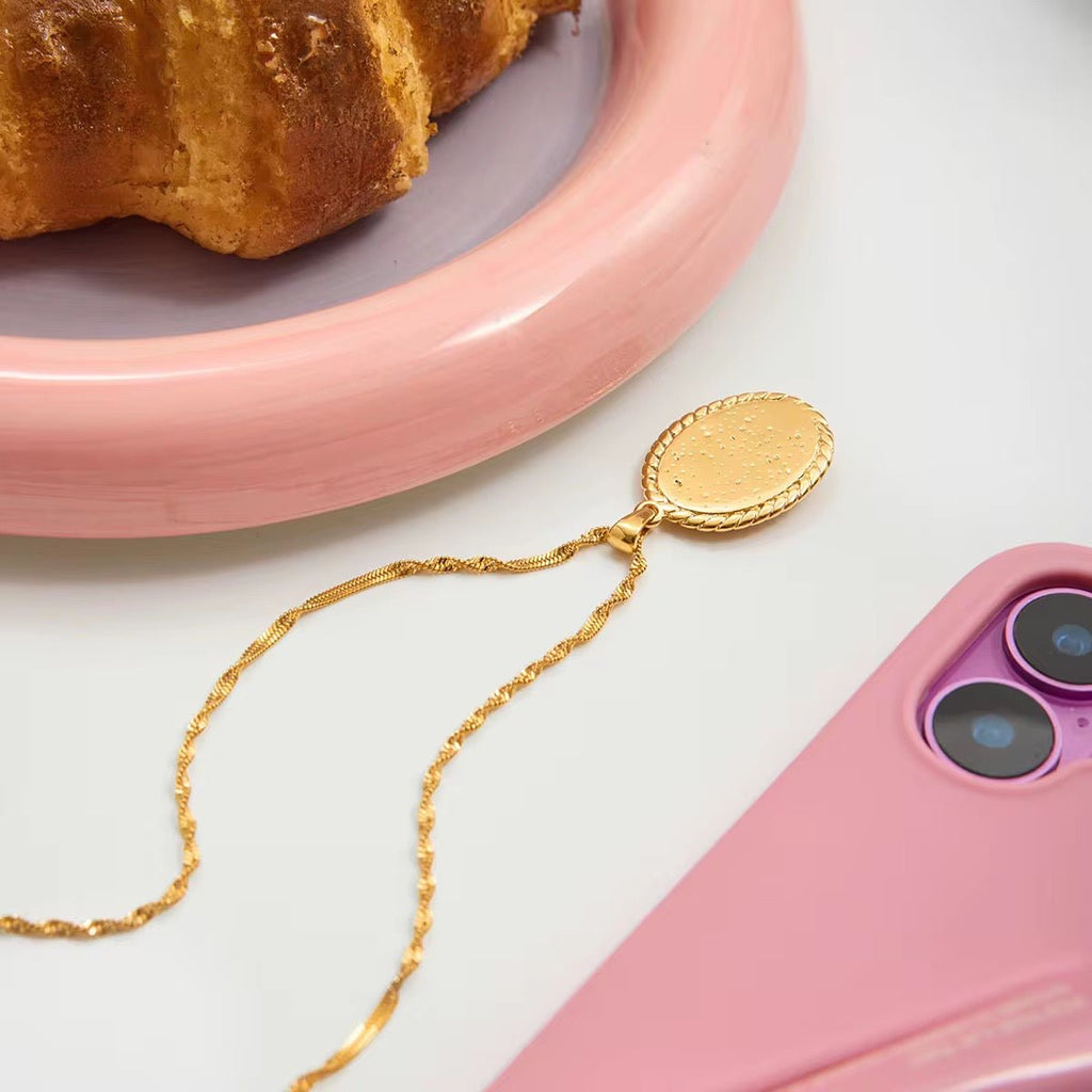 Gold phone chain on a pink phone with a croissant on a pink plate in the background