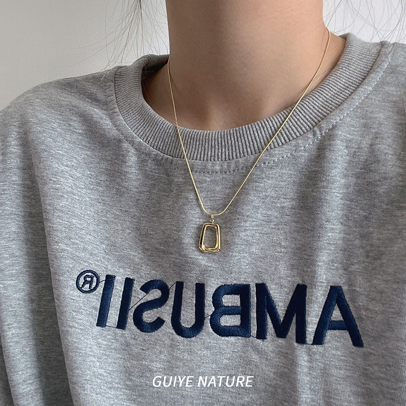 Person wearing a gray sweatshirt with 'Ambush' branding and a gold necklace.