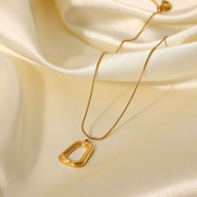 Gold necklace with a rectangular pendant on a beige fabric background