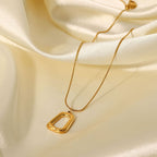 Gold necklace with a rectangular pendant on a beige fabric background