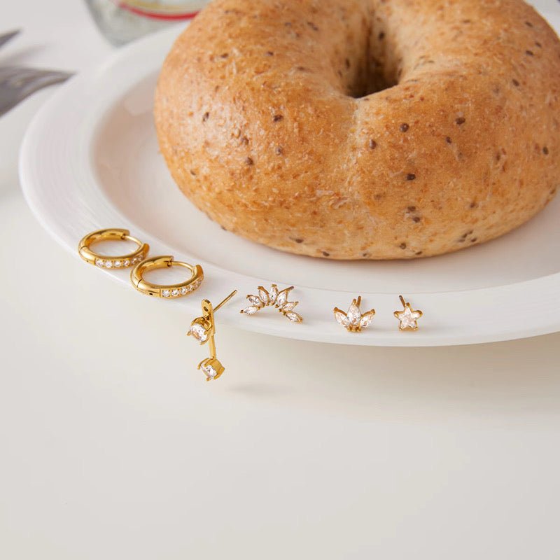 Gold earrings on a white plate with a bagel