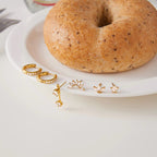 Gold earrings on a white plate with a bagel
