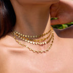 Close-up of a person wearing multiple gold necklaces with a blurred natural background