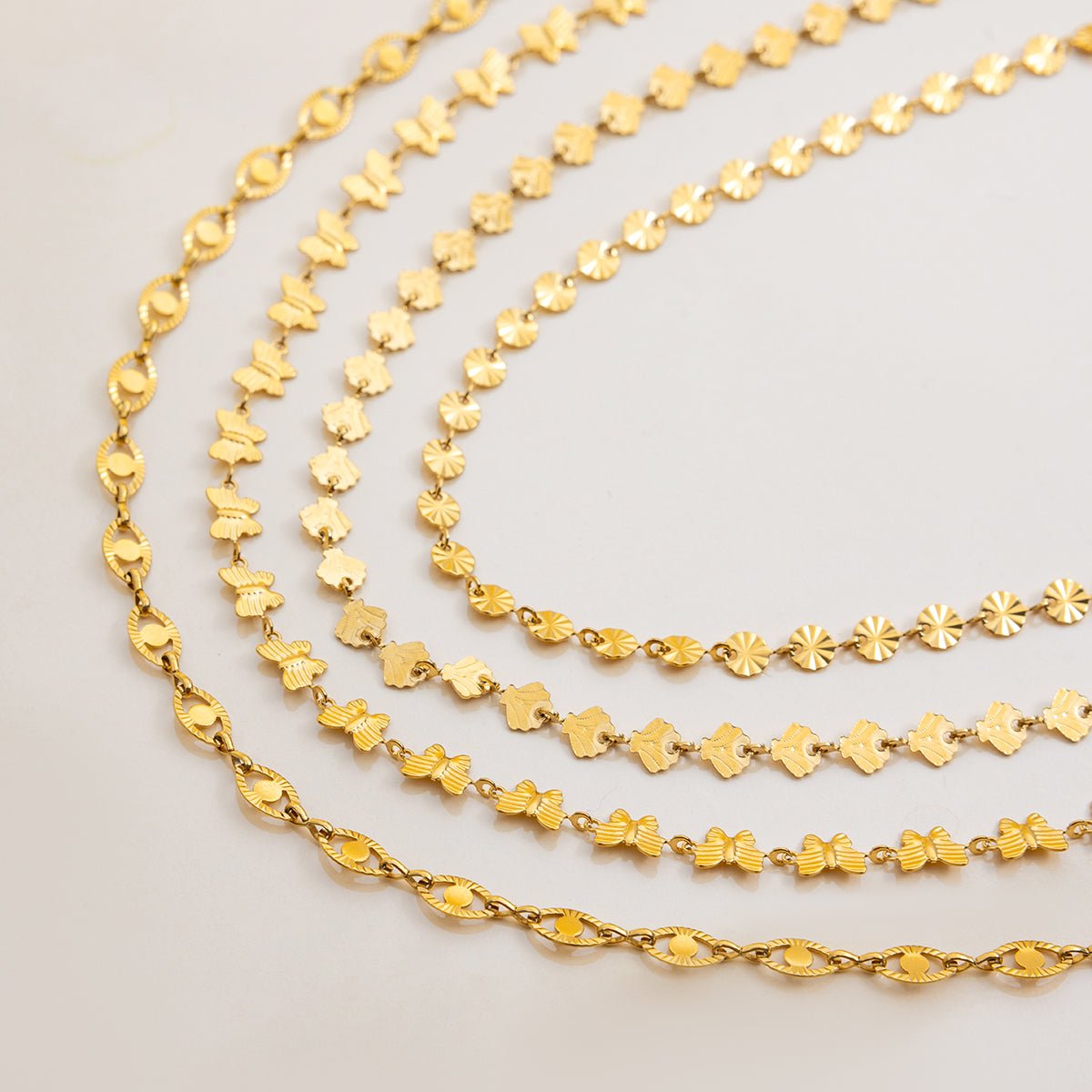 Three gold chains of different designs on a light gray background