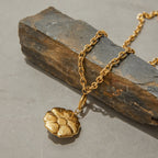 Gold chain necklace with a floral pendant on a stone surface