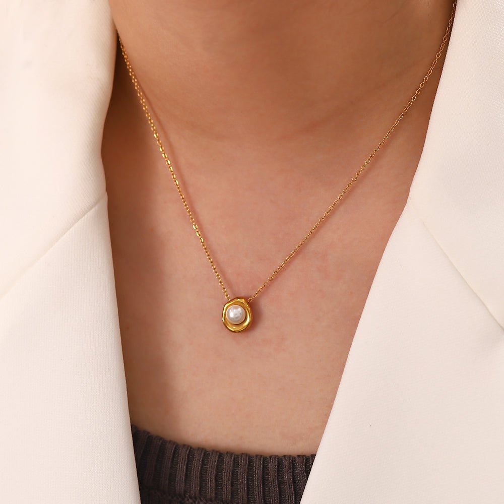 Gold necklace with a pearl pendant worn by a person in a beige jacket.