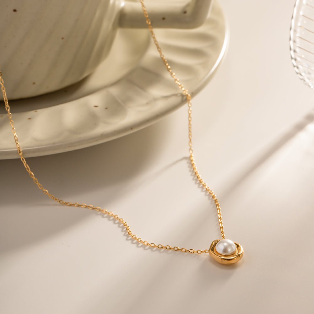 Gold necklace with a pearl pendant on a neutral background