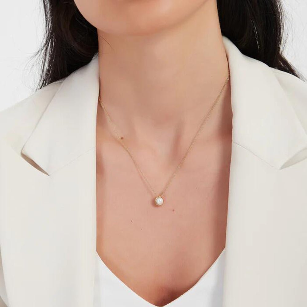 Gold necklace with a pearl pendant worn by a person in a white blazer.
