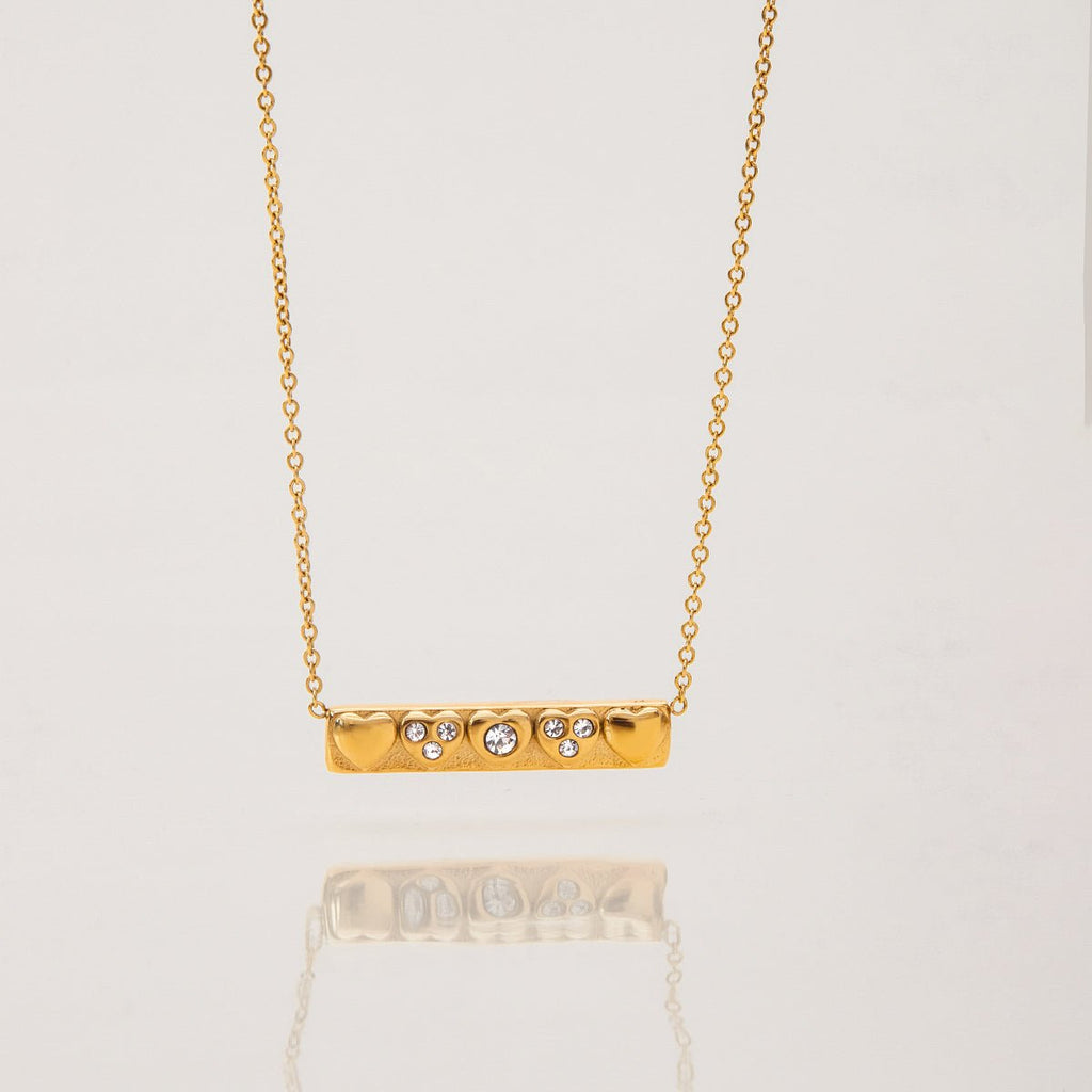 Gold necklace with a bar pendant featuring small diamonds on a light gray background