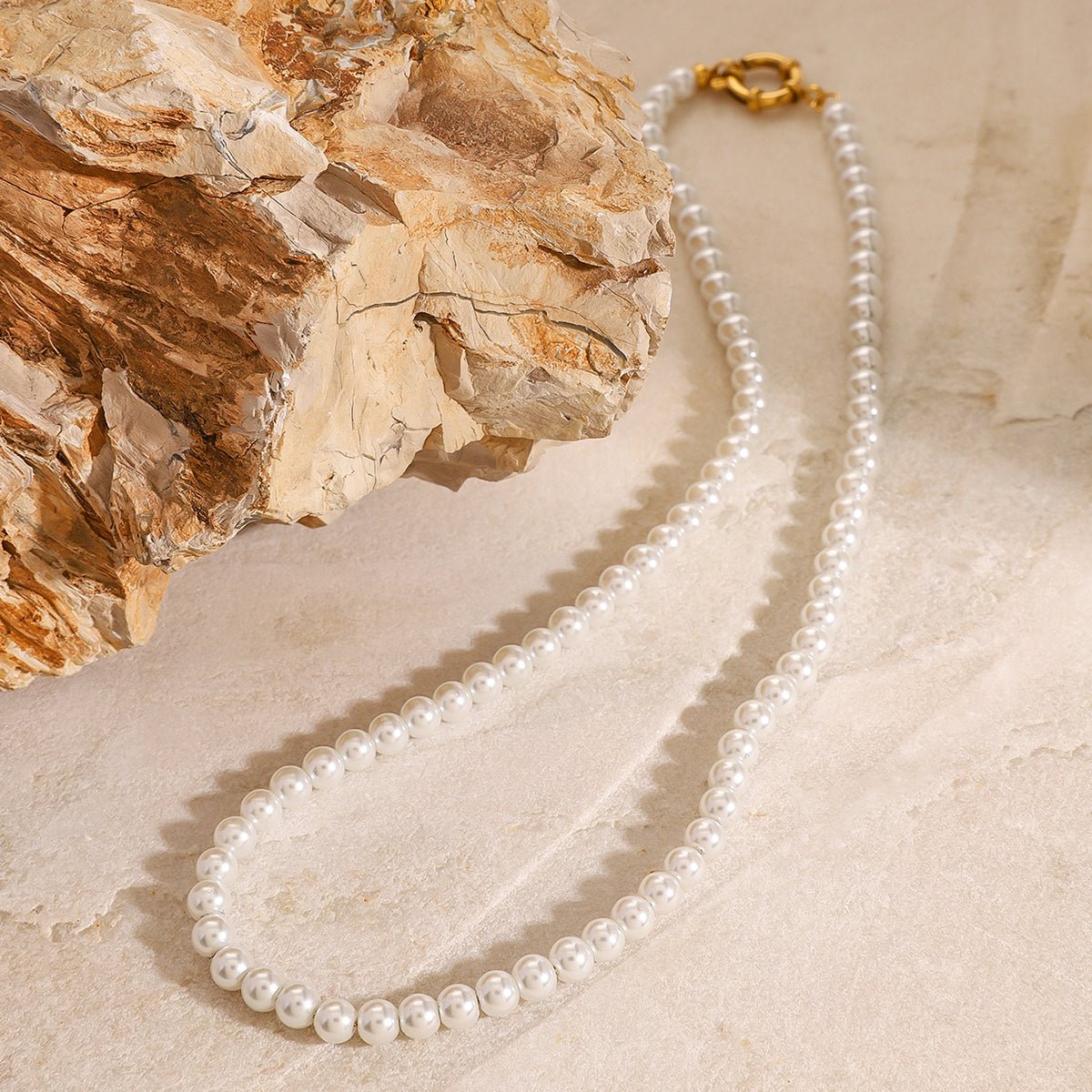 Pearl necklace with a gold clasp on a textured beige surface