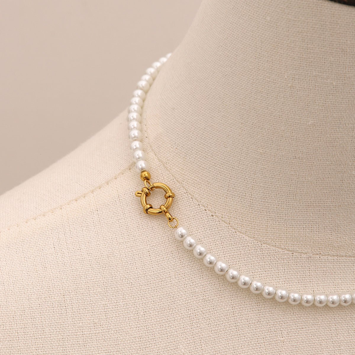 Pearl necklace with a gold clasp on a mannequin bust.