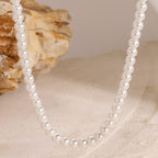 Pearl necklace on a textured beige surface with a shell in the background
