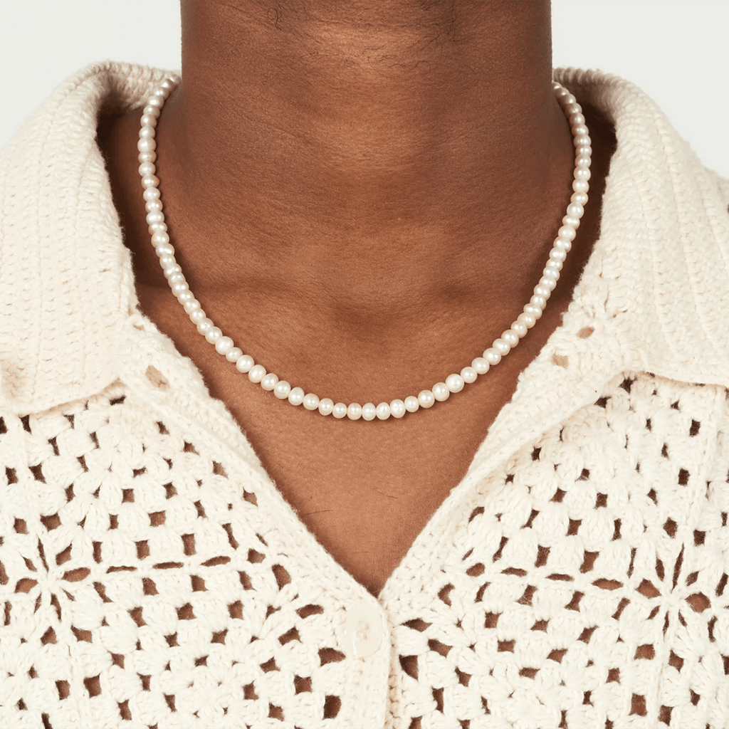 Pearl necklace worn by a person with a beige crochet top on a white background