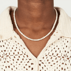 Pearl necklace worn by a person with a beige crochet top on a white background