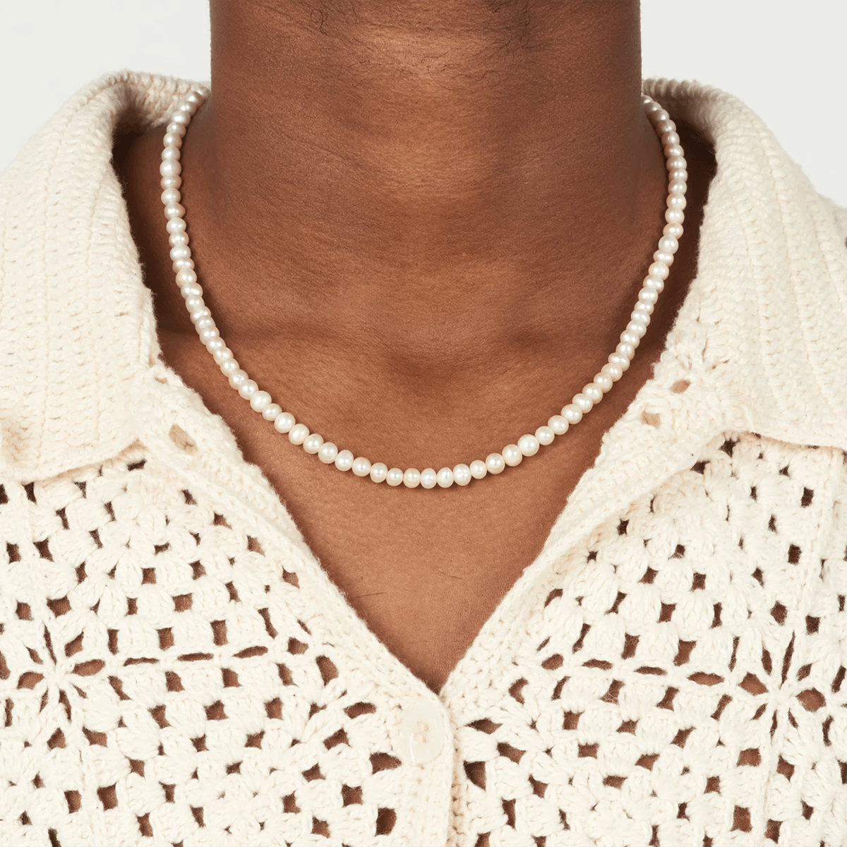 Pearl necklace worn by a person with a beige crochet top on a white background