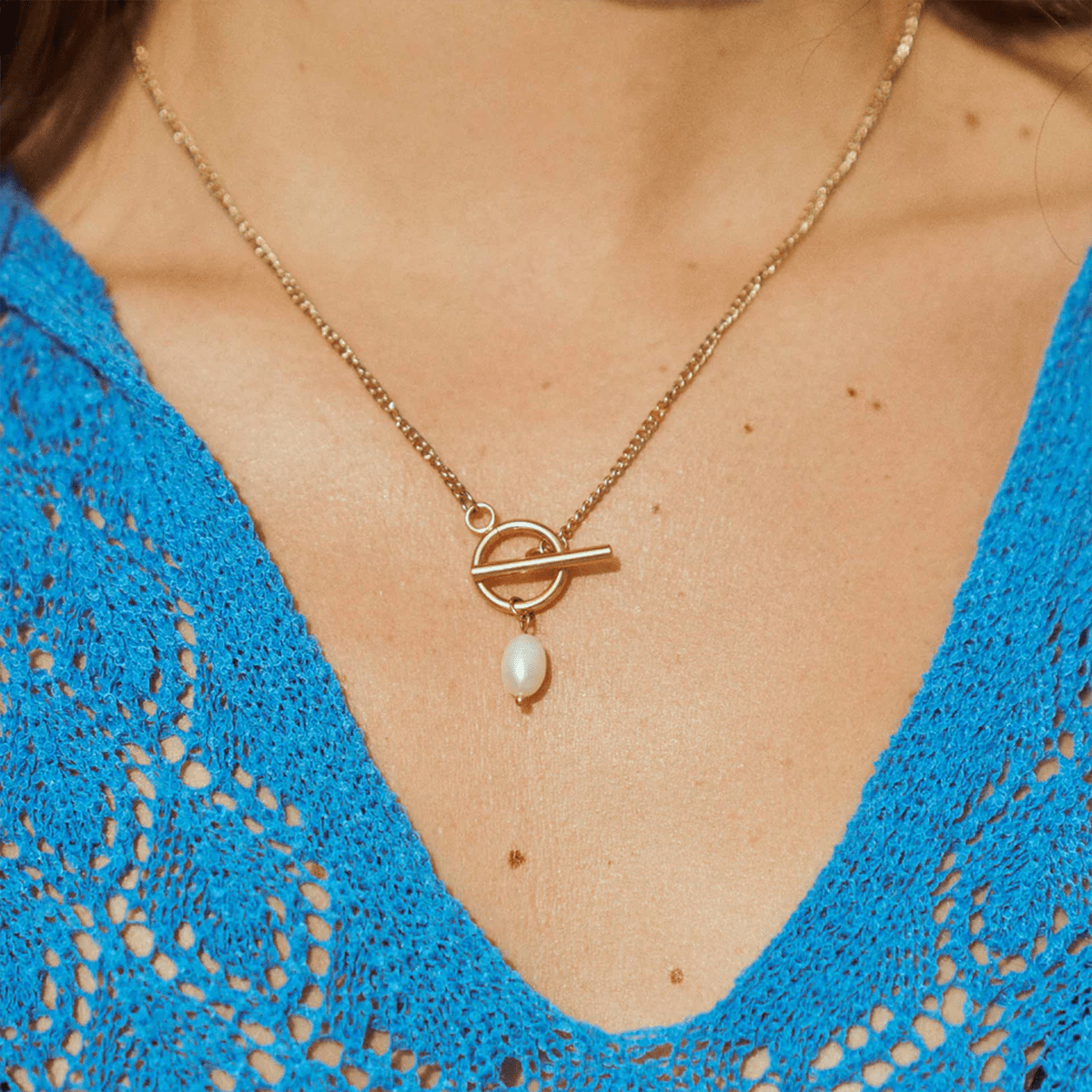 Gold necklace with a pendant worn by a person in a blue top
