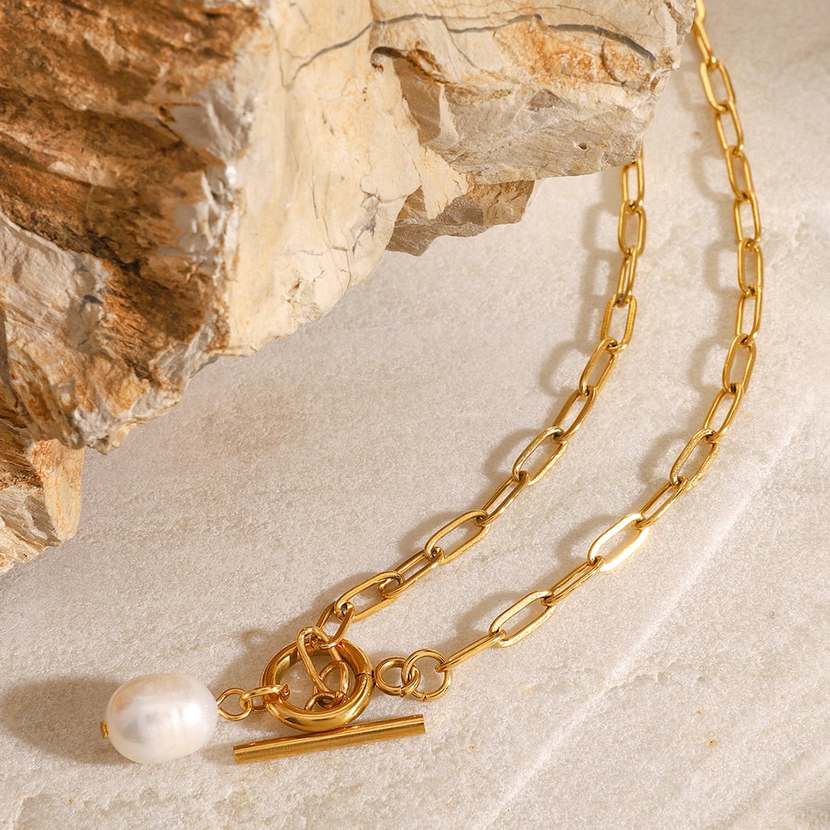 Gold chain necklace with a pearl pendant on a stone surface