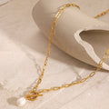 Gold chain necklace with a pearl pendant on a beige surface