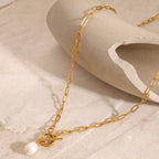 Gold chain necklace with a pearl pendant on a beige surface