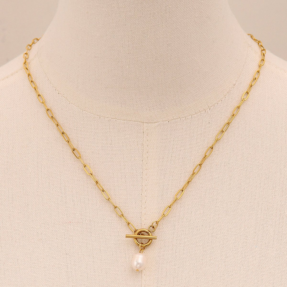 Gold necklace with a pearl pendant on a mannequin bust.