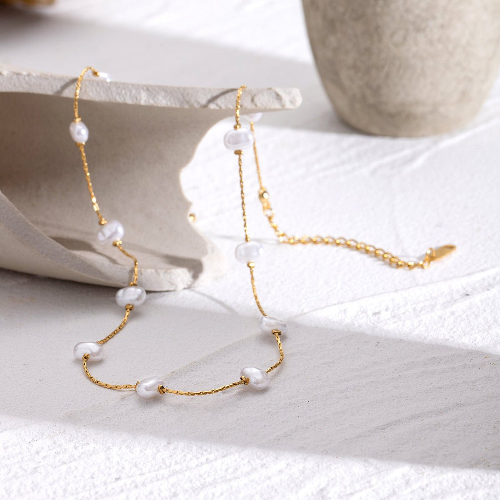 Gold necklace with pearls on a white surface