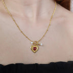Gold necklace with a heart-shaped pendant featuring a red gemstone and pearl on a person's neck.