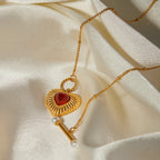 Gold necklace with a heart-shaped pendant and red stone on a beige fabric background