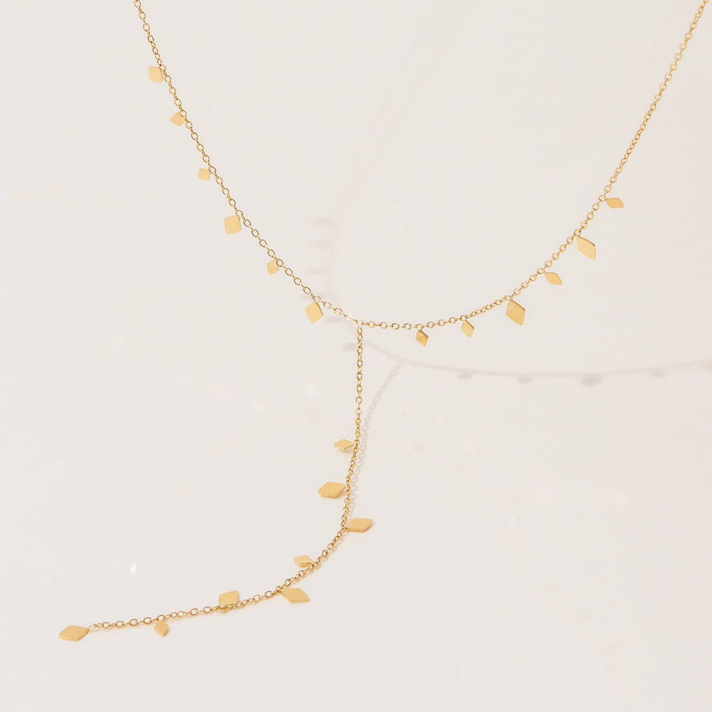 Gold necklace with leaf-shaped pendants on a light beige background
