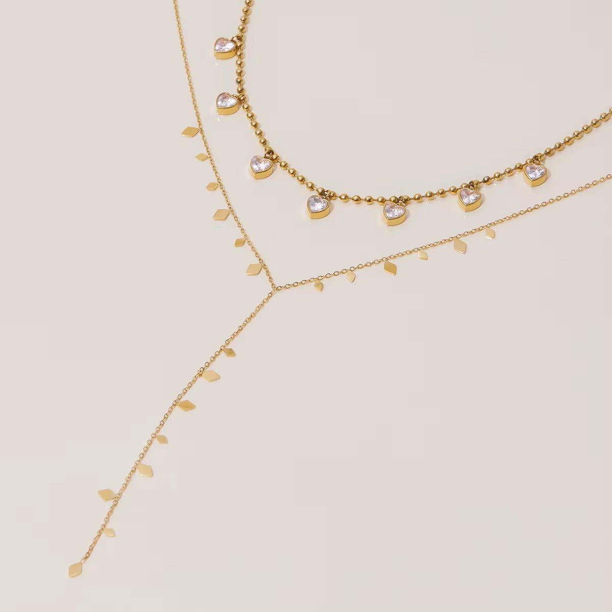 Two gold necklaces with small beads on a beige background