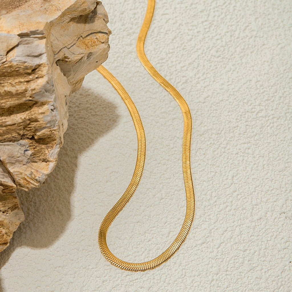 Gold snake-shaped necklace on a textured beige surface with a stone-like background