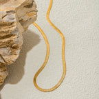 Gold snake-shaped necklace on a textured beige surface with a stone-like background