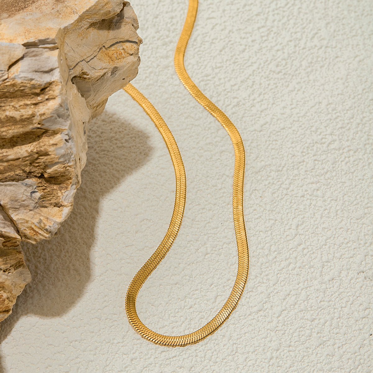 Gold snake-shaped necklace on a textured beige surface with a stone-like background