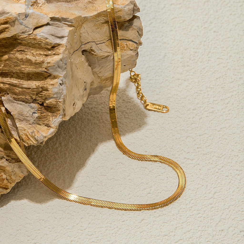 Gold chain necklace on a textured beige surface with a stone block background