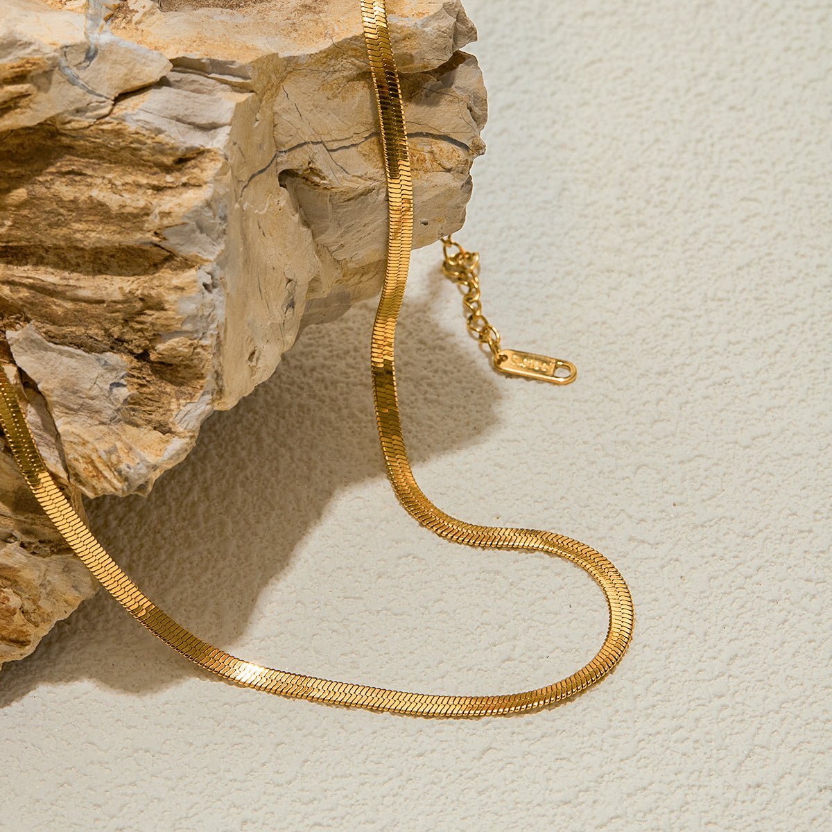 Gold chain necklace on a textured beige surface with a stone block background