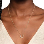 Gold necklace with a unique pendant on a person wearing a beige top.