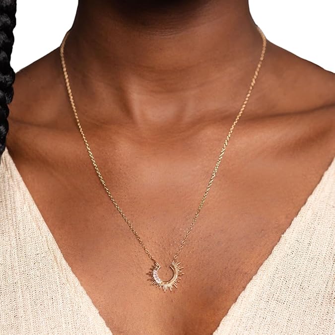 Gold necklace with a unique pendant on a person wearing a beige top.