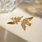 Gold bird-shaped earrings on a beige surface with a crystal object in the background