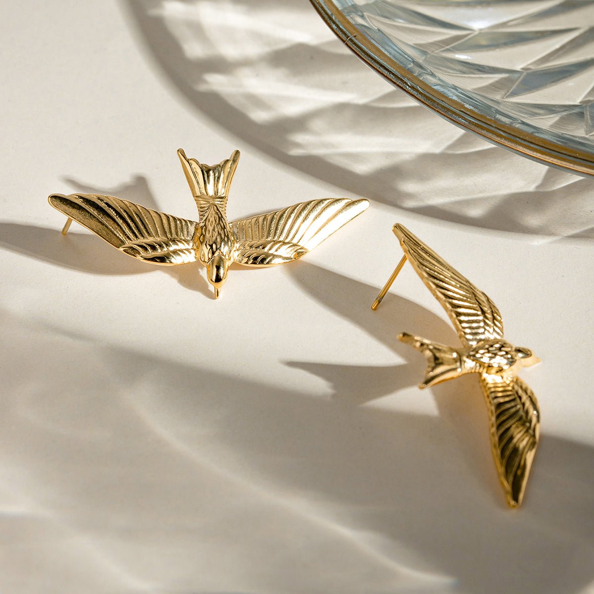 Gold bird-shaped earrings on a neutral background