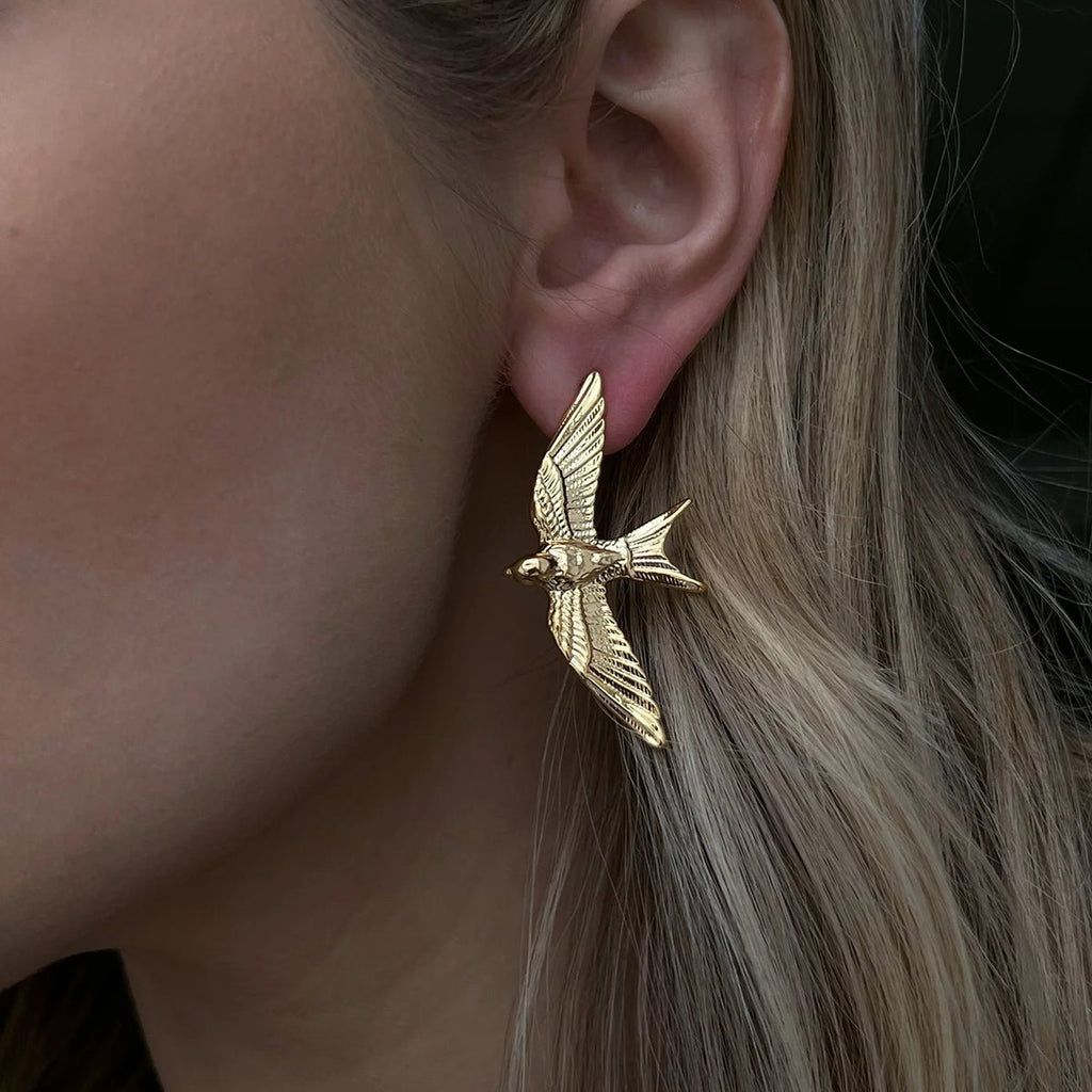 Gold bird-shaped earring worn by a person with blonde hair.
