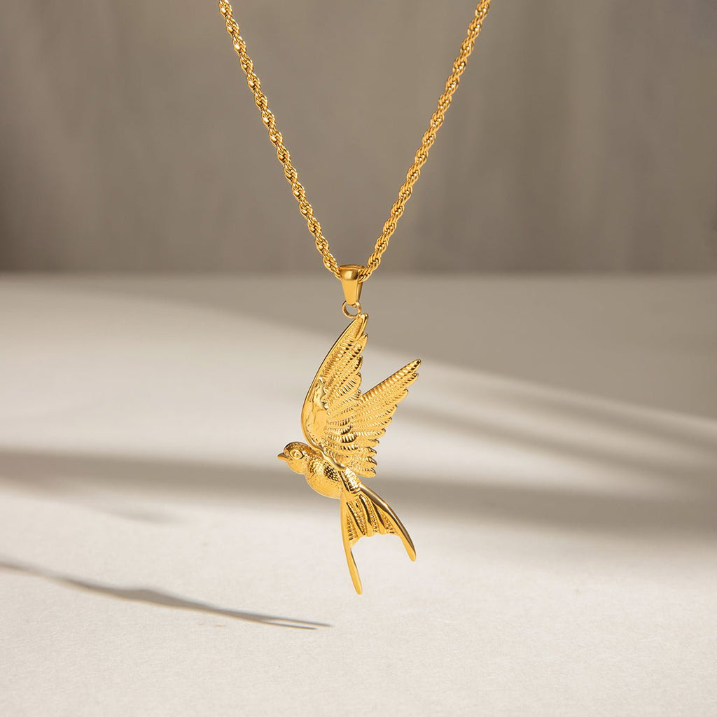 Gold bird pendant necklace on a neutral background