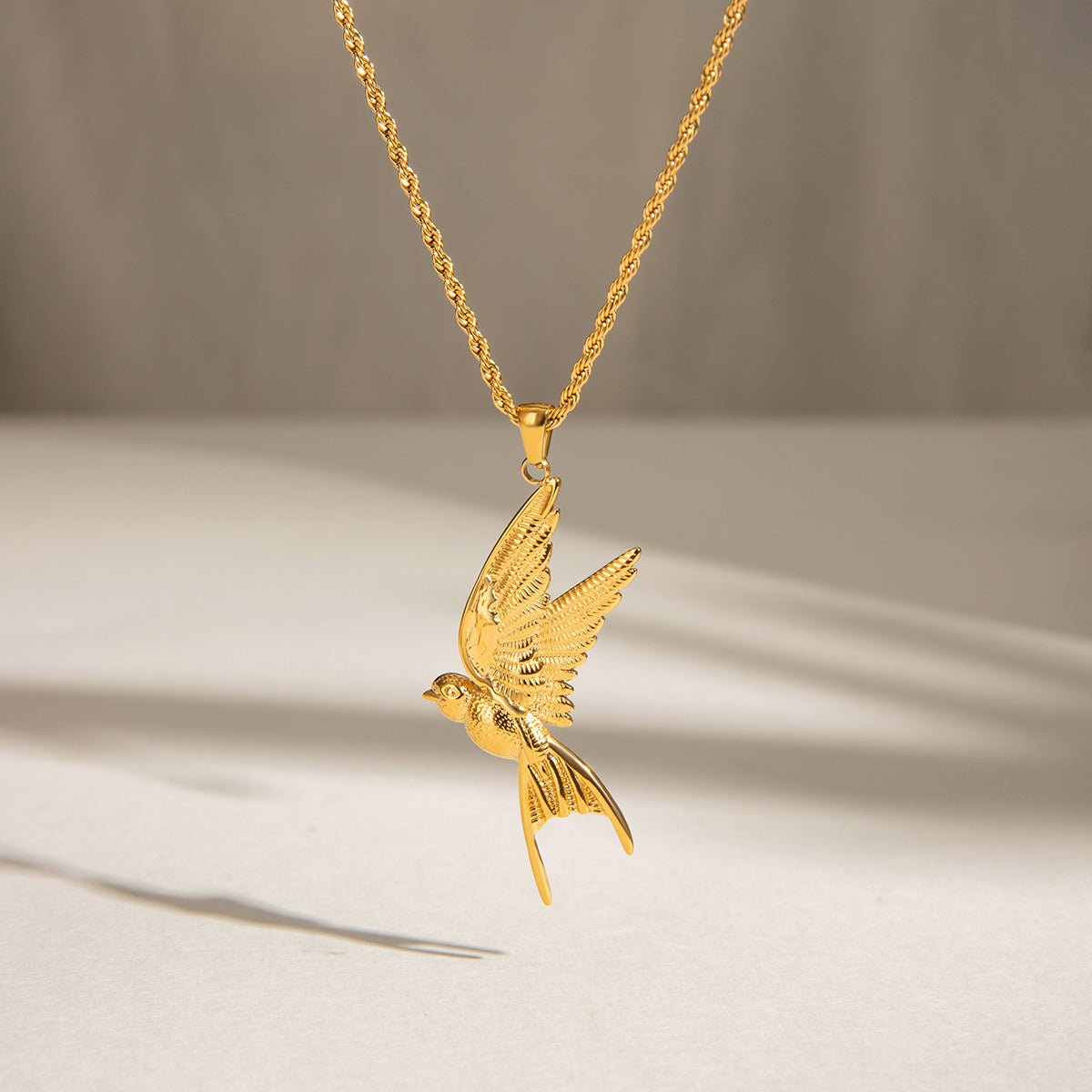 Gold bird pendant necklace on a neutral background