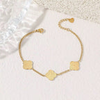 Gold bracelet with clover-shaped charms on a textured white surface