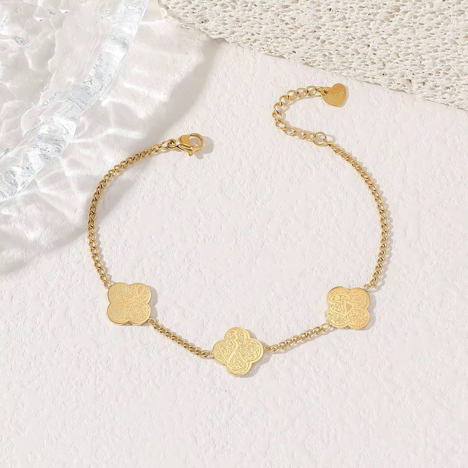 Gold bracelet with clover-shaped charms on a textured white surface