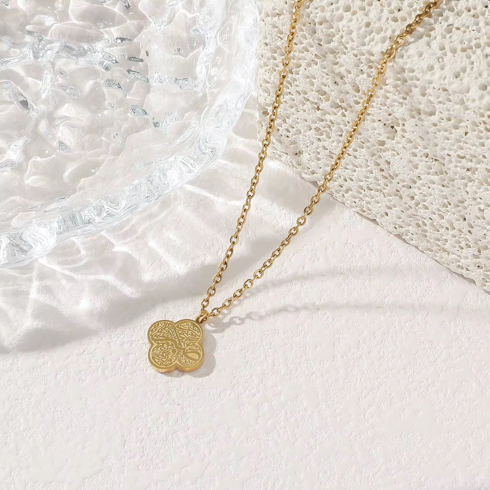 Gold necklace with a floral pendant on a textured white surface