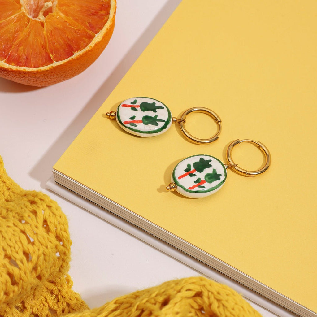 Keychains with vegetable design on a yellow surface next to a notebook and orange.