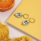 Keychains with vegetable design on a yellow surface next to a notebook and orange.