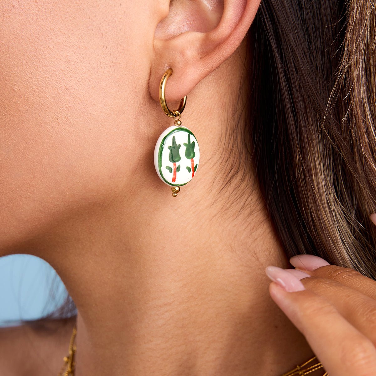 Close-up of a person wearing a gold hoop earring with a colorful pendant.