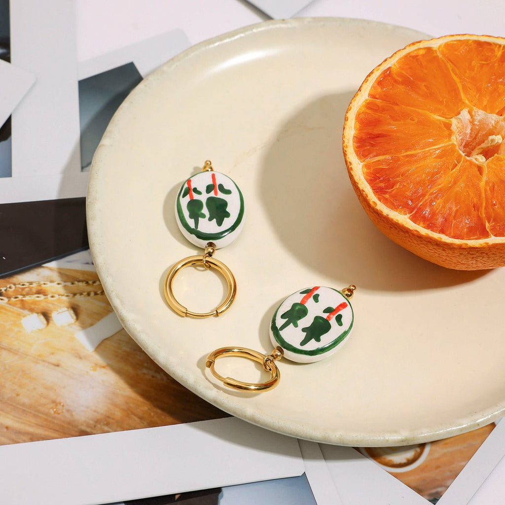 Pair of earrings with green and red design on a white plate with an orange half.