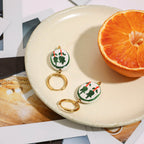 Pair of earrings with green and red design on a white plate with an orange half.