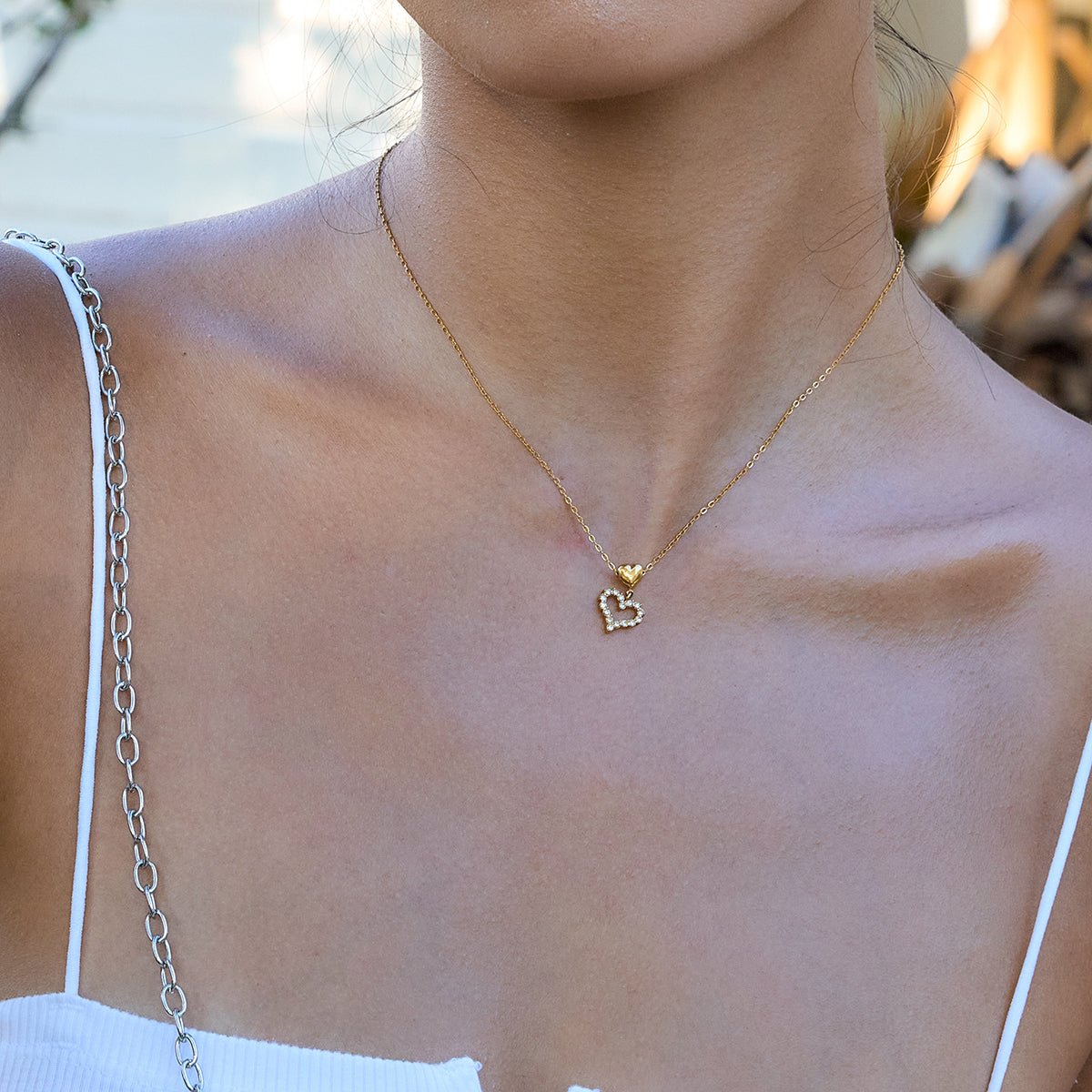 Gold necklace with a heart pendant worn by a person outdoors